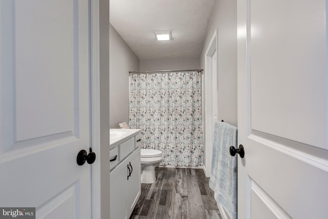 bathroom featuring a shower with shower curtain, wood finished floors, toilet, and vanity