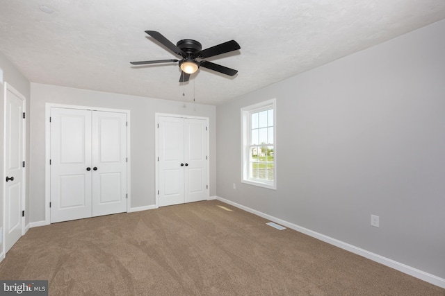 unfurnished bedroom with two closets, ceiling fan, baseboards, carpet flooring, and visible vents