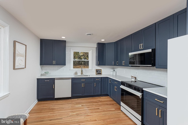 kitchen featuring sink, blue cabinets, tasteful backsplash, white appliances, and light wood-type flooring