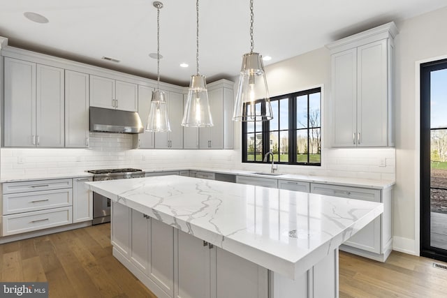 kitchen featuring light wood-type flooring, stainless steel stove, a kitchen island, and light stone counters