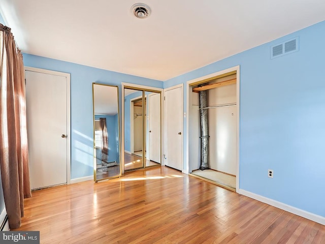 unfurnished bedroom with two closets and light hardwood / wood-style floors