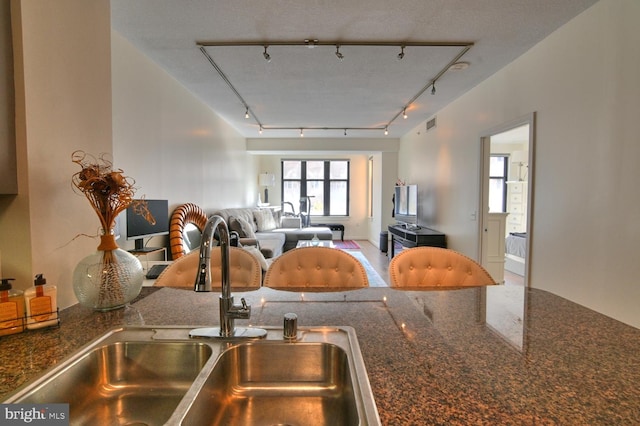 kitchen with a textured ceiling, rail lighting, dark stone countertops, and sink