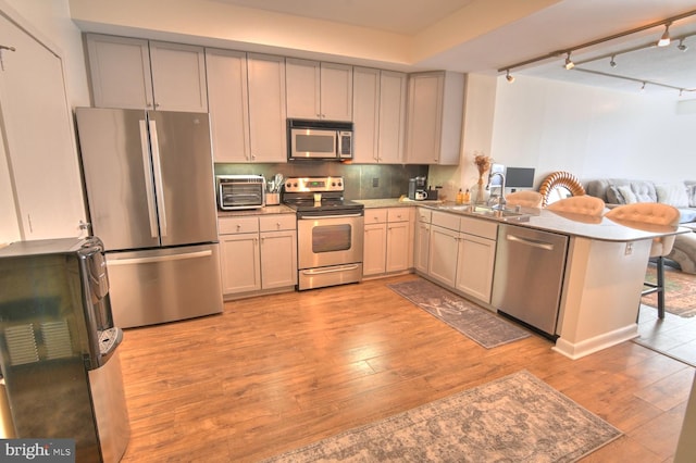 kitchen featuring kitchen peninsula, appliances with stainless steel finishes, light wood-type flooring, a kitchen breakfast bar, and sink