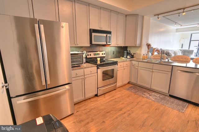 kitchen featuring track lighting, sink, decorative backsplash, light wood-type flooring, and appliances with stainless steel finishes