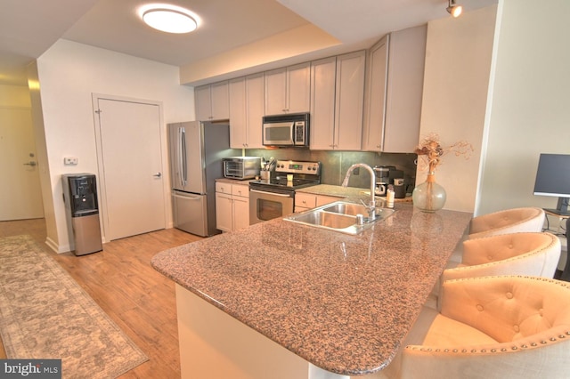 kitchen featuring sink, decorative backsplash, appliances with stainless steel finishes, light hardwood / wood-style floors, and kitchen peninsula