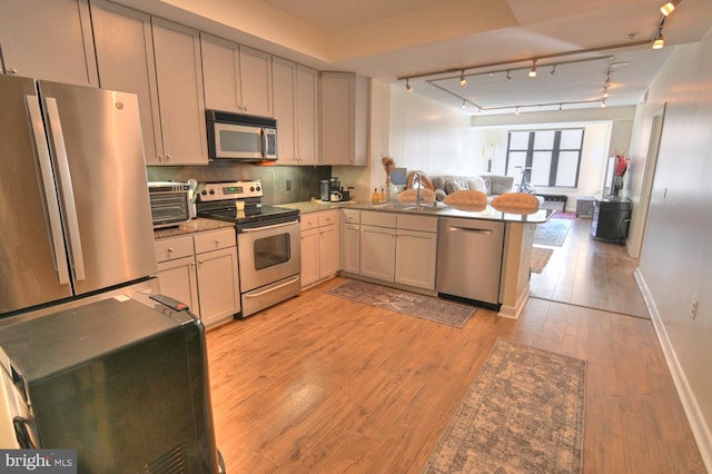 kitchen featuring backsplash, sink, light hardwood / wood-style floors, kitchen peninsula, and stainless steel appliances