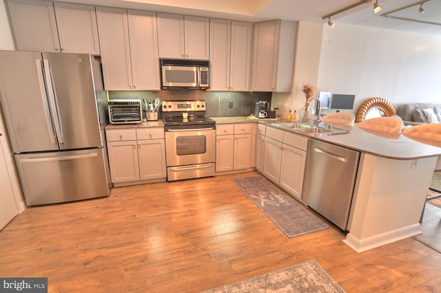 kitchen featuring backsplash, sink, light wood-type flooring, kitchen peninsula, and stainless steel appliances