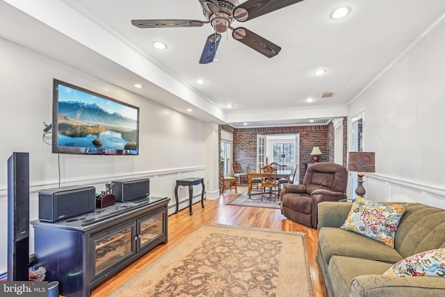 living room featuring hardwood / wood-style flooring, ceiling fan, ornamental molding, and brick wall