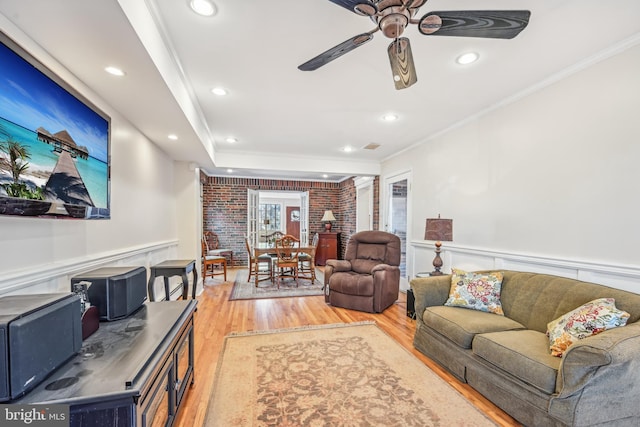 living room featuring wood-type flooring, ceiling fan, crown molding, and brick wall