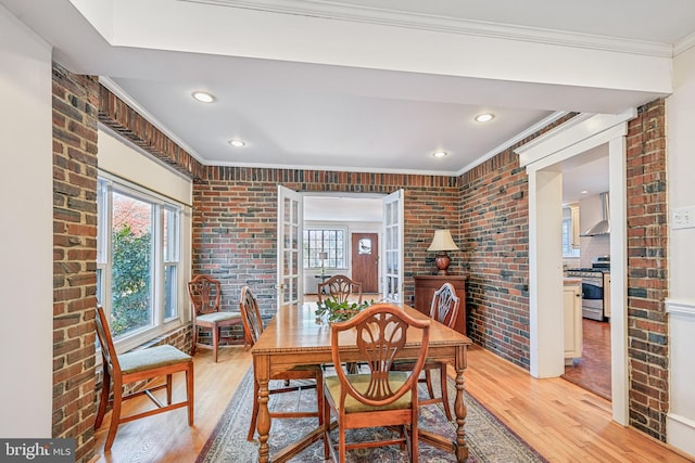 dining space with ornamental molding, brick wall, and light wood-type flooring