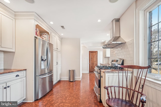 kitchen featuring wall chimney exhaust hood, decorative backsplash, dark stone countertops, appliances with stainless steel finishes, and white cabinetry