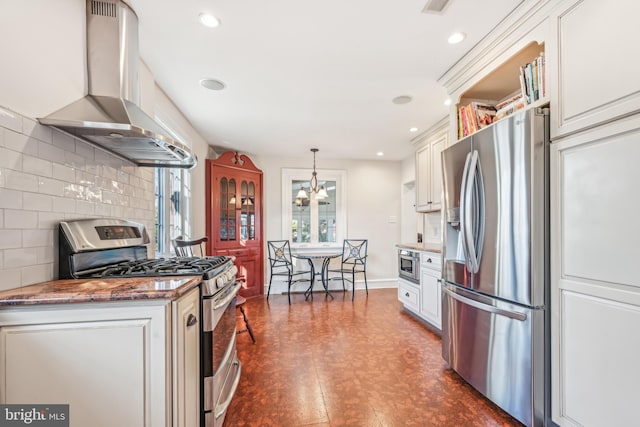 kitchen with backsplash, wall chimney range hood, hanging light fixtures, appliances with stainless steel finishes, and white cabinetry