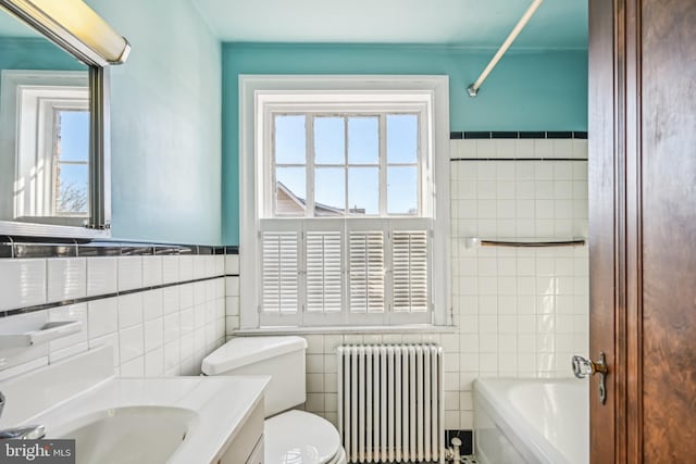 bathroom with a wealth of natural light, radiator, a bathing tub, and tile walls