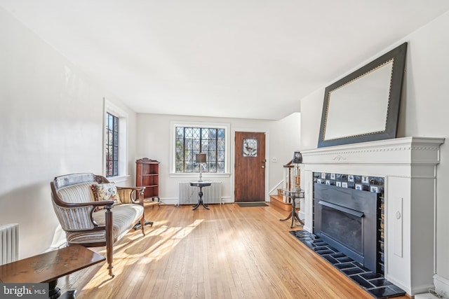 sitting room with radiator heating unit, light wood-type flooring, and a tiled fireplace