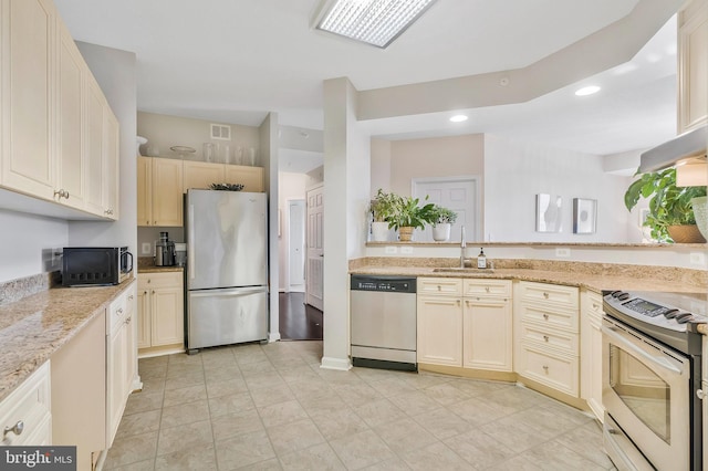 kitchen with cream cabinetry, sink, light stone countertops, and stainless steel appliances