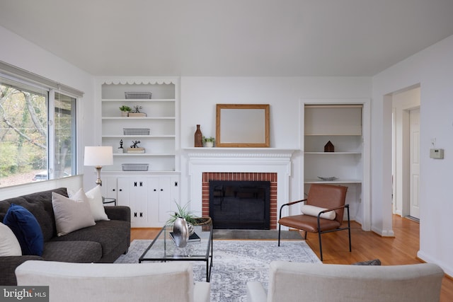 living room featuring built in shelves, light hardwood / wood-style floors, and a brick fireplace