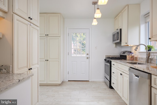 kitchen featuring light stone countertops, appliances with stainless steel finishes, sink, decorative light fixtures, and light hardwood / wood-style floors