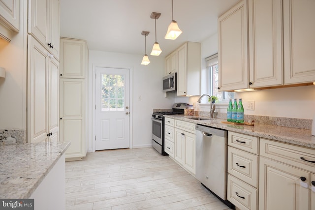 kitchen featuring appliances with stainless steel finishes, light stone counters, sink, decorative light fixtures, and light hardwood / wood-style floors