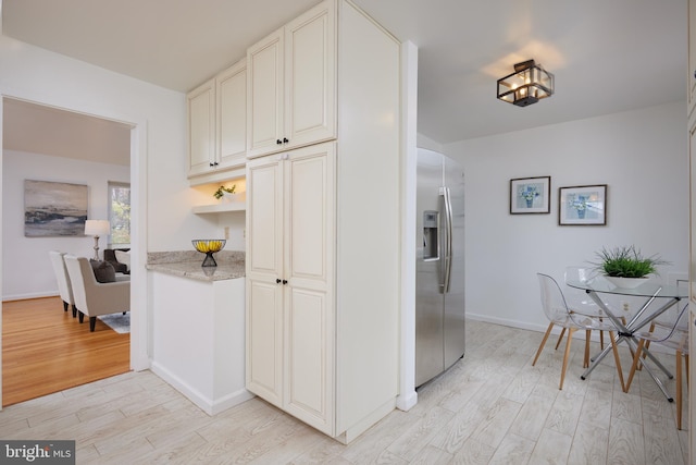 kitchen featuring light stone countertops, stainless steel fridge, light wood-type flooring, and white cabinets