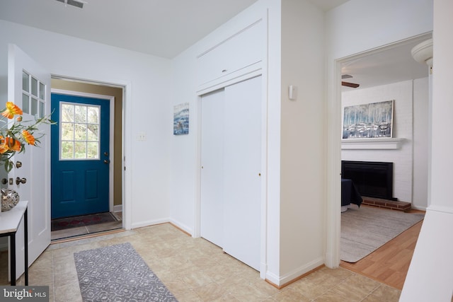 foyer entrance with light hardwood / wood-style floors, a brick fireplace, and ceiling fan