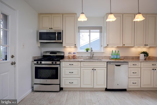 kitchen with hanging light fixtures, sink, stainless steel appliances, and light hardwood / wood-style flooring