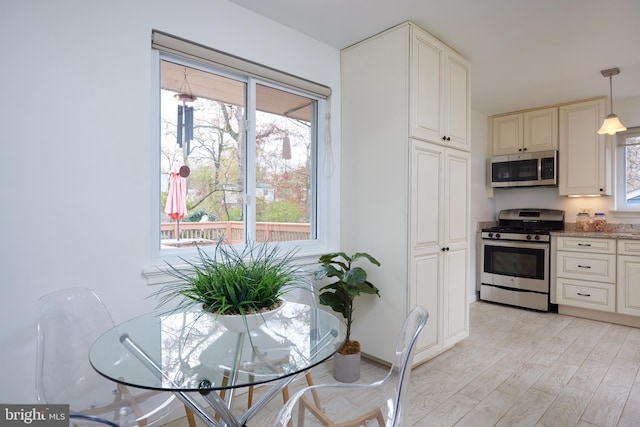 kitchen featuring pendant lighting, light stone counters, stainless steel appliances, and light hardwood / wood-style flooring