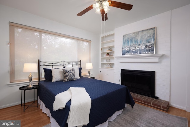 bedroom with ceiling fan, wood-type flooring, and a fireplace