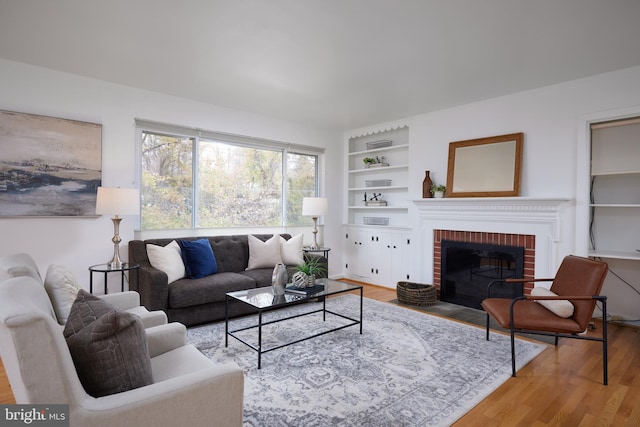 living room with wood-type flooring, a brick fireplace, and built in shelves