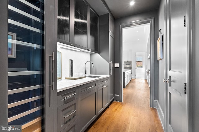 bar featuring light stone countertops, sink, stainless steel oven, backsplash, and light wood-type flooring