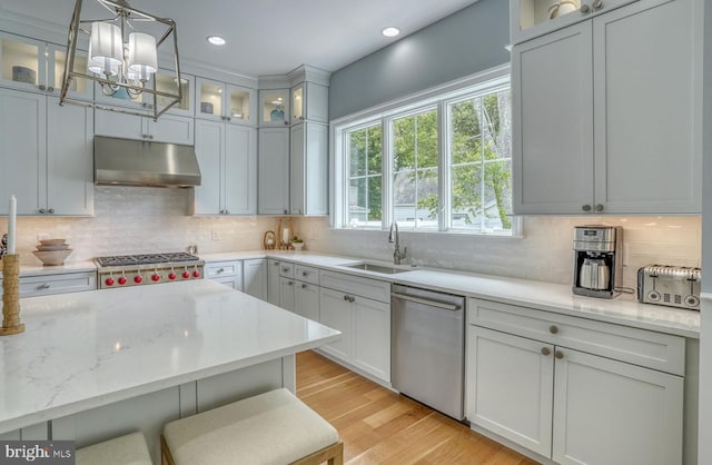 kitchen featuring sink, appliances with stainless steel finishes, decorative light fixtures, light hardwood / wood-style floors, and light stone counters