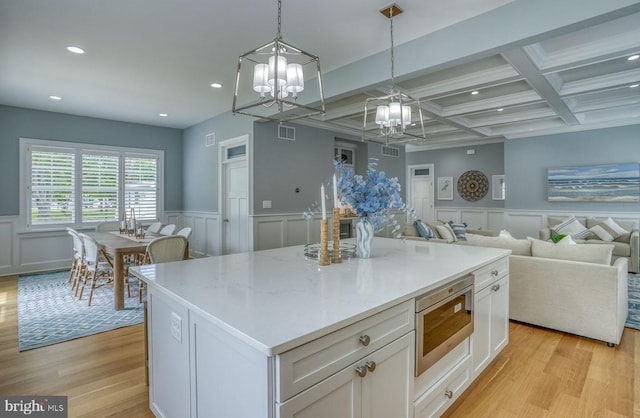 kitchen with beamed ceiling, white cabinetry, a kitchen island, and light hardwood / wood-style floors