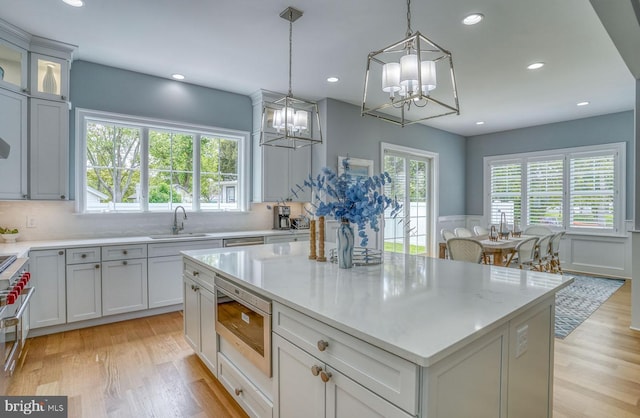 kitchen with light stone countertops, light wood-type flooring, sink, pendant lighting, and a center island