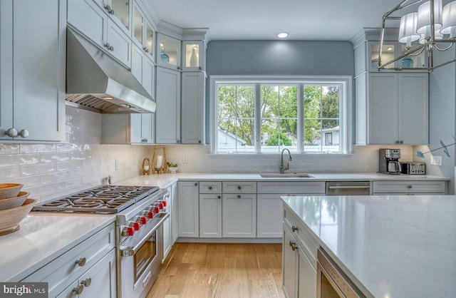 kitchen featuring sink, hanging light fixtures, high end stainless steel range oven, backsplash, and light hardwood / wood-style floors