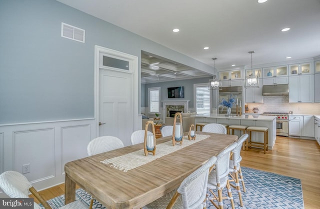 dining space with a fireplace, beam ceiling, and light hardwood / wood-style flooring