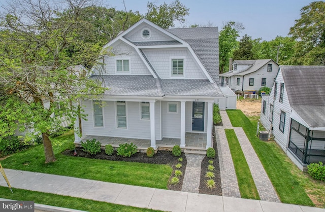 view of front of house featuring covered porch, central AC unit, and a front yard