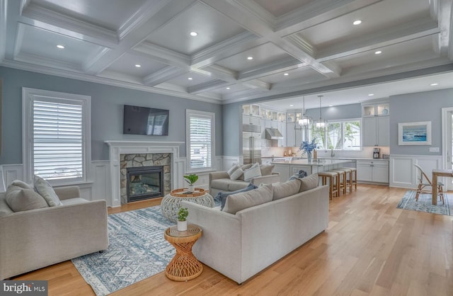 living room featuring beamed ceiling, light wood-type flooring, a stone fireplace, and ornamental molding