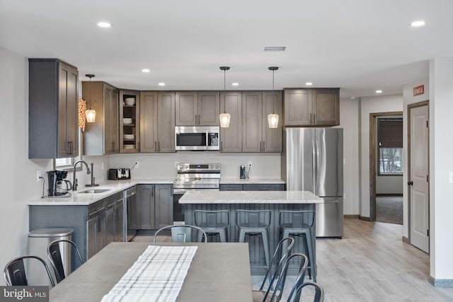 kitchen with sink, a kitchen island, hanging light fixtures, appliances with stainless steel finishes, and light wood-type flooring