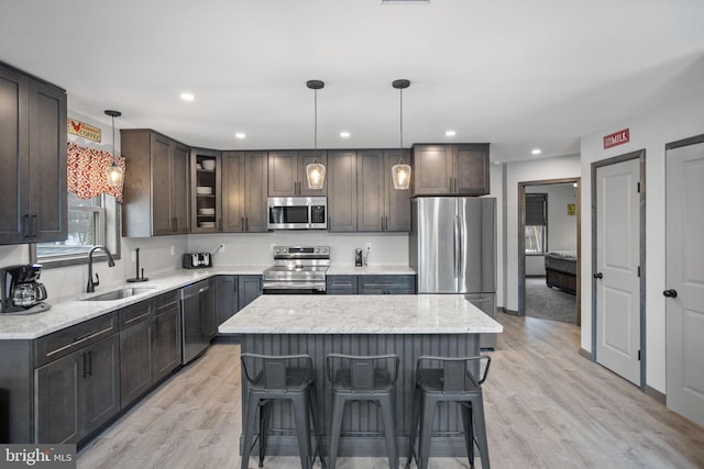 kitchen with sink, hanging light fixtures, a center island, light wood-type flooring, and stainless steel appliances