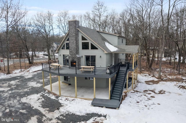 snow covered house with a patio and a wooden deck