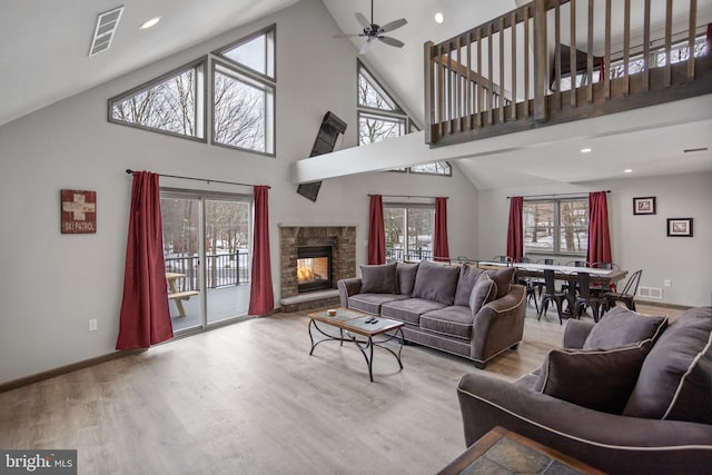 living room featuring a fireplace, light hardwood / wood-style flooring, high vaulted ceiling, and ceiling fan