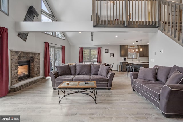 living room featuring a fireplace, high vaulted ceiling, sink, and light hardwood / wood-style floors