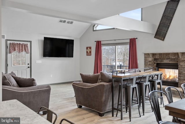 living room with light hardwood / wood-style flooring, plenty of natural light, vaulted ceiling with beams, and a stone fireplace