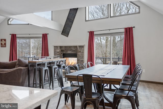 dining space featuring a fireplace, a wealth of natural light, high vaulted ceiling, and light hardwood / wood-style flooring