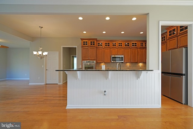 kitchen with appliances with stainless steel finishes, pendant lighting, light hardwood / wood-style flooring, and a kitchen breakfast bar