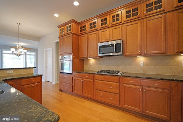 kitchen featuring decorative light fixtures, light wood-type flooring, appliances with stainless steel finishes, tasteful backsplash, and a notable chandelier