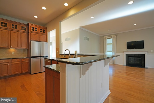 kitchen with stainless steel refrigerator, light hardwood / wood-style flooring, dark stone countertops, a breakfast bar area, and ornamental molding