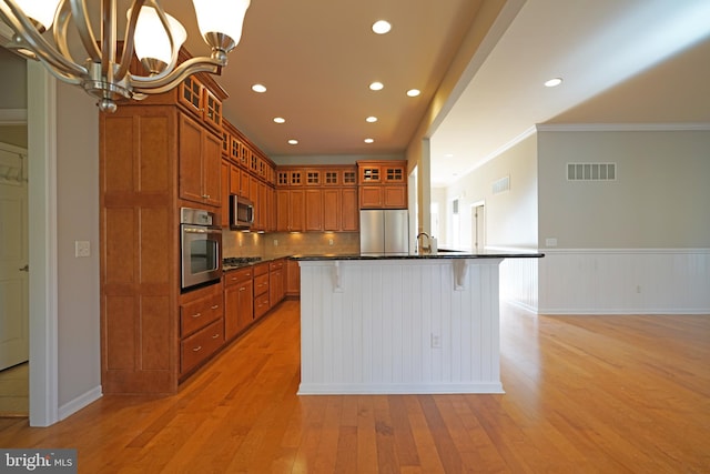 kitchen featuring light hardwood / wood-style flooring, an island with sink, a kitchen bar, appliances with stainless steel finishes, and ornamental molding