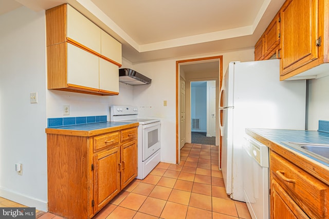 kitchen featuring white appliances, a tray ceiling, exhaust hood, tile counters, and light tile patterned flooring