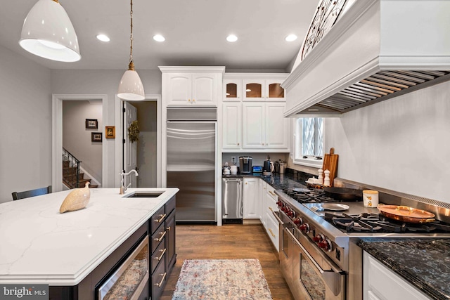 kitchen with custom exhaust hood, high quality appliances, dark stone countertops, white cabinets, and hanging light fixtures