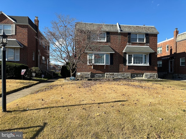 view of front facade with brick siding, mansard roof, and a front lawn